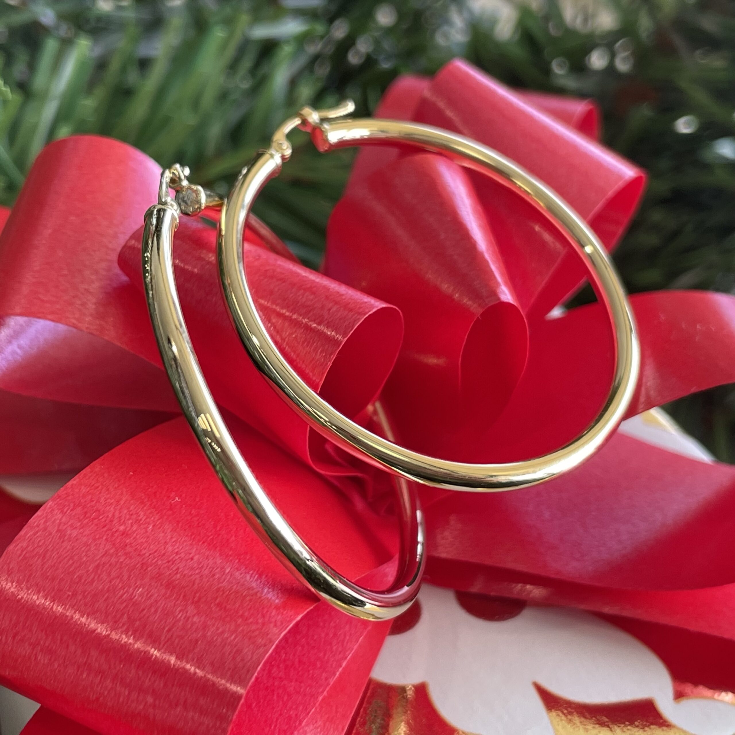Yellow Gold Hoop Earrings resting on a red bow with green garland in the background