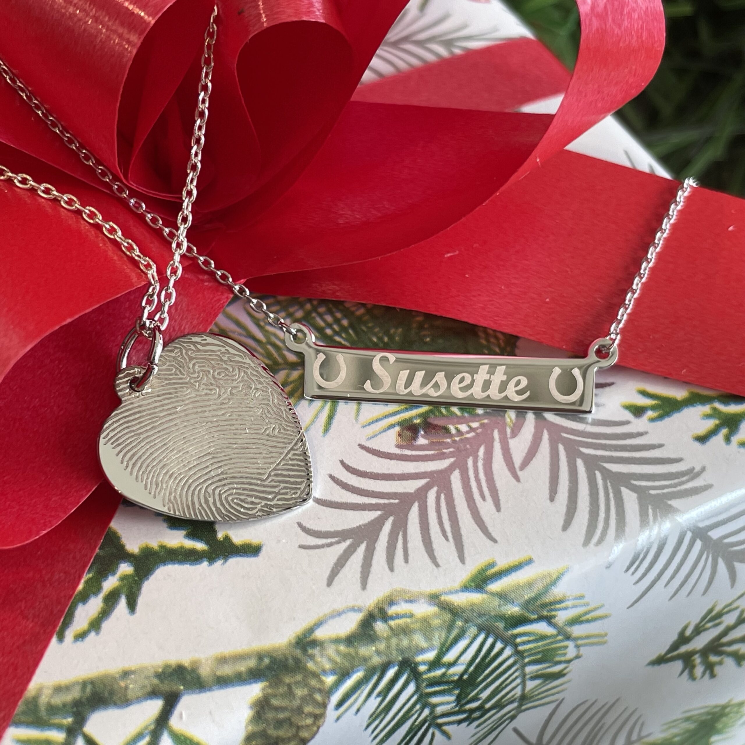 Silver heart pendant with fingerprint pattern and personalized Susette name plat necklace a top a wrapped present